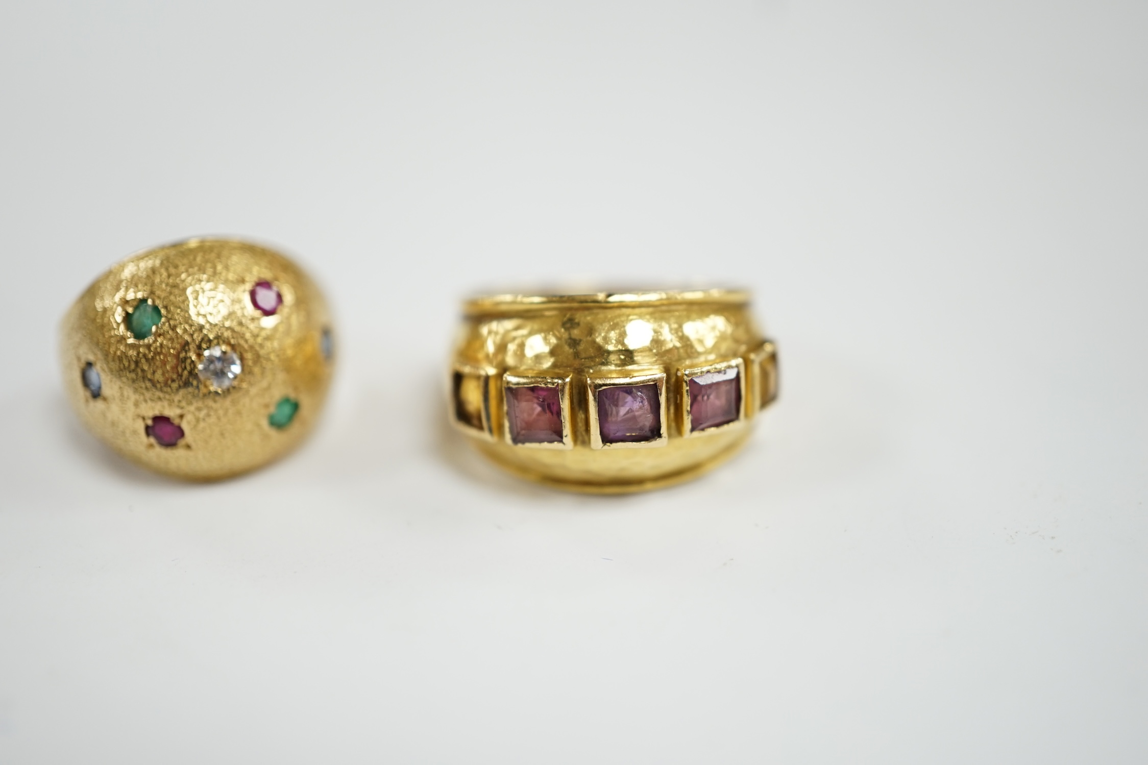 A textured yellow metal, emerald, ruby and diamond set domed ring, size K, together with a stylish yellow metal and graduated square cut amethyst set five stone ring, size M, gross weight 13.1 grams.